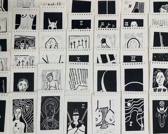 May include: A collection of black and white linocut prints, each depicting a different image. The prints are arranged in rows on a white surface. Some of the images include a cross, a bird, a crescent moon, a skull, and a human figure.