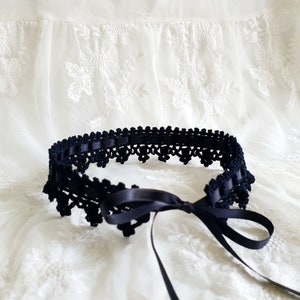 May include: A black crocheted garter belt with a satin ribbon tie. The garter belt is delicate and intricate, with a scalloped edge.