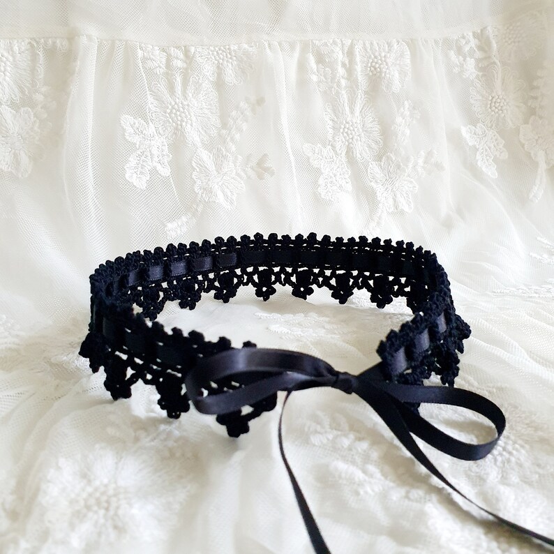 May include: A black crocheted garter belt with a satin ribbon tie. The garter belt is delicate and intricate, with a scalloped edge.