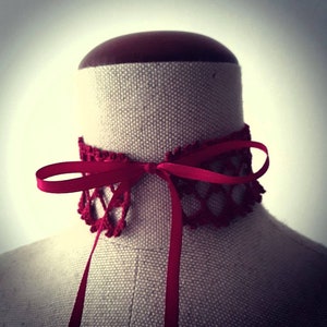 May include: A red crocheted choker with a red satin ribbon tied in a bow.