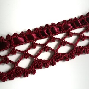 May include: Burgundy crochet trim with a satin ribbon woven through the center. The trim has a delicate, lacy design.