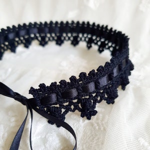 May include: Black crochet choker with a satin ribbon tie. The choker is made of delicate black lace and has a scalloped edge.