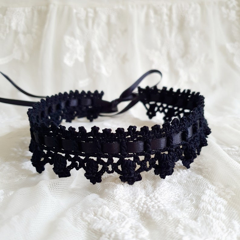 May include: Black lace choker with a satin ribbon tie. The choker is made of delicate crocheted lace and features a black satin ribbon that ties at the back of the neck.