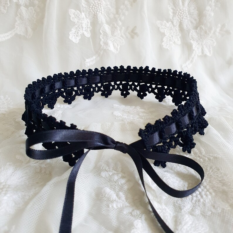May include: Black crocheted choker with a satin ribbon tie. The choker is made of delicate lace and has a simple, elegant design.