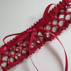 May include: A red crocheted garter with a satin ribbon bow. The garter is made with a delicate lace pattern.