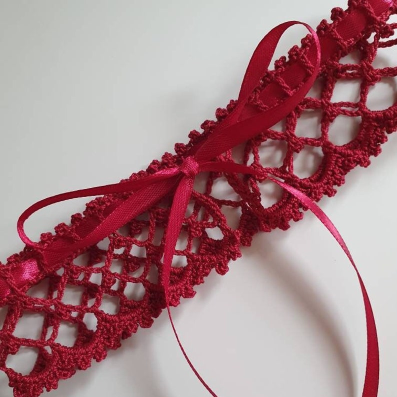 May include: A red crocheted garter with a satin ribbon bow. The garter is made with a delicate lace pattern.