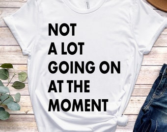 May include: White t-shirt with the text "NOT A LOT GOING ON AT THE MOMENT" printed in black.