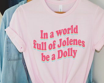 May include: A pink t-shirt with the text "In a world full of Jolenes be a Dolly" in a rainbow font.