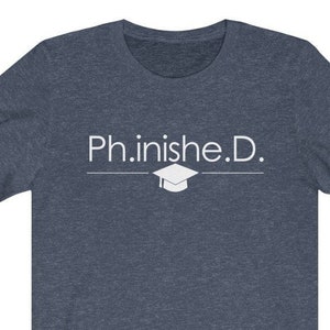 Può includere: Una maglietta blu scuro con il testo "Ph.inished.D." in bianco, con un'icona di cappello di laurea sotto.