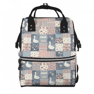 Może przedstawiać: Plecak w stylu patchwork z kwiatowymi wzorami, gęsiami i motylami. Kwadraty są w pastelowych odcieniach różu, błękitu i bieli. Posiada czarne uchwyty i paski oraz przednią kieszeń na zamek. Design jest uroczy.