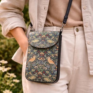 May include: A black crossbody phone bag with a flap closure. The bag features a colorful floral and bird pattern on a dark blue background. The strap is black.