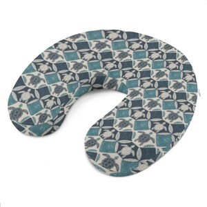 May include: A U-shaped travel pillow with a repeating pattern of turtles in white, teal, and navy blue. The pillow is designed for neck support and comfort, featuring a soft, patterned fabric.