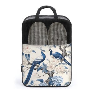 May include: A black travel bag with a handle, featuring a mesh top section and a decorative front panel. The panel displays a blue and white peacock design with floral accents. The bag contains two grey and white striped slippers.