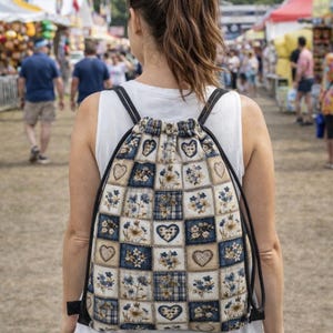 May include: A drawstring backpack with a patchwork design. The bag features squares of blue plaid, floral patterns, and heart shapes in shades of blue, beige, and white. The backpack has black straps and a drawstring closure.