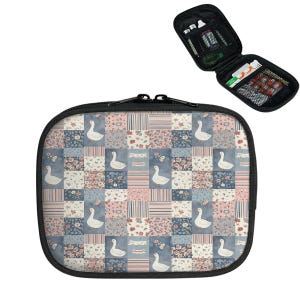 May include: A black zippered travel case with a patchwork design featuring white geese, floral patterns, and blue and pink squares. The case is open, revealing mesh pockets and small items. A second, open case is visible.