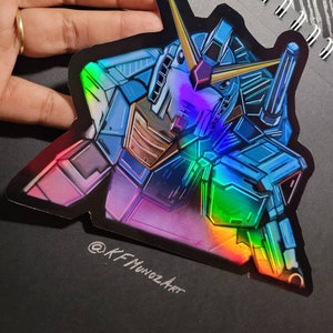 Puede incluir: Una pegatina hologr&aacute;fica con una ilustraci&oacute;n detallada de un robot azul y verde con un acabado iridiscente arco&iacute;ris. La pegatina tiene un fondo negro y el texto "@KFMunozArt" es visible en la parte inferior.