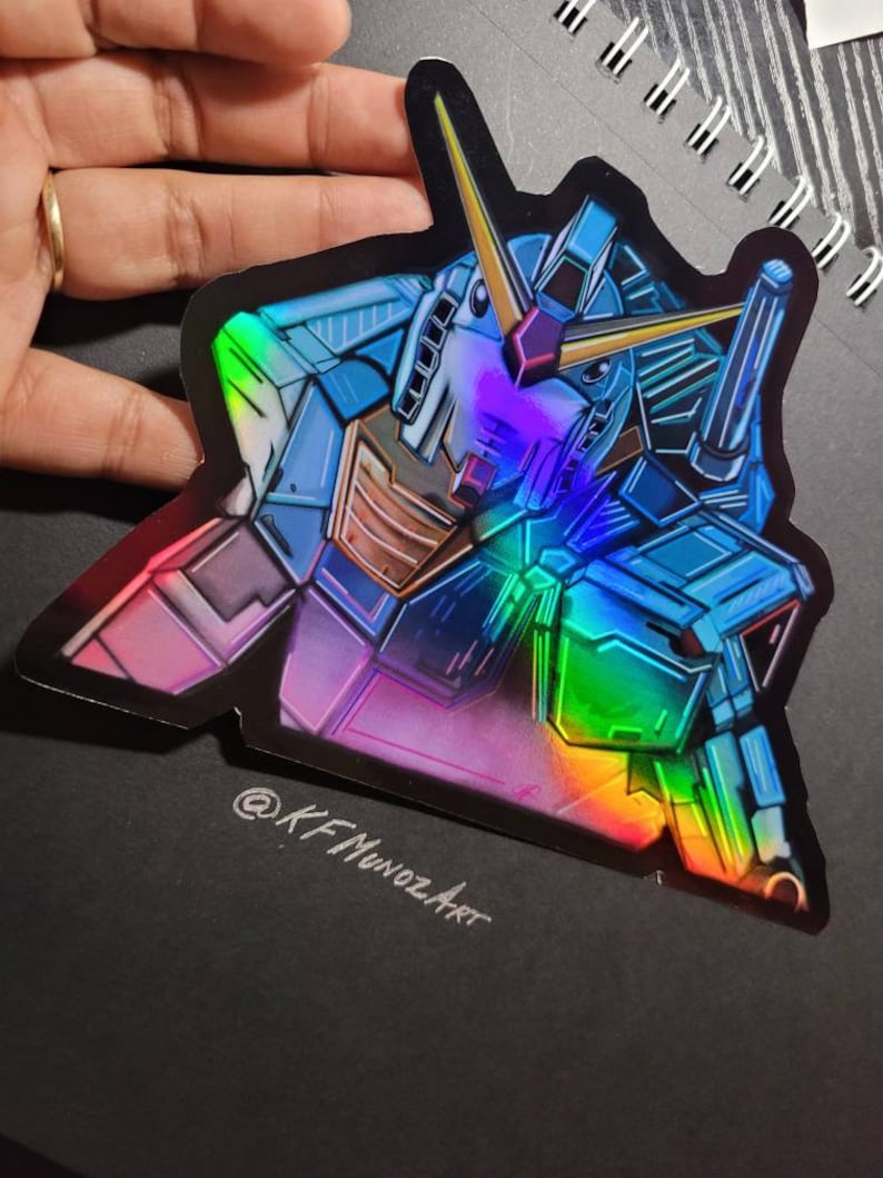 Puede incluir: Una pegatina hologr&aacute;fica con una ilustraci&oacute;n detallada de un robot azul y verde con un acabado iridiscente arco&iacute;ris. La pegatina tiene un fondo negro y el texto "@KFMunozArt" es visible en la parte inferior.