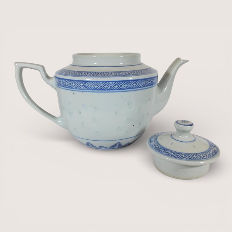 May include: White porcelain teapot with blue geometric patterns and a matching lid. The teapot has a curved handle and a spout. The lid is round with a small knob. The teapot is a classic design.