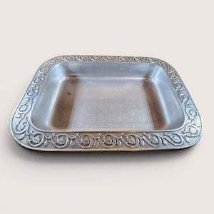May include: A rectangular, silver-colored metal tray with rounded corners. The tray's border features a detailed floral and leaf pattern. The interior of the tray is smooth and reflective, suitable for serving or display.
