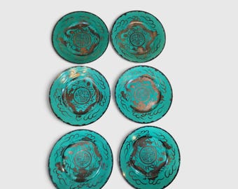 May include: A set of six round plates in a vibrant turquoise color, each featuring a central circular emblem with intricate gold-toned calligraphy and stylized dragon motifs encircling the center, finished with a decorative scalloped edge.