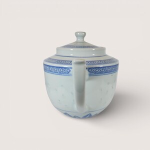 May include: A white porcelain teapot with a blue geometric pattern around the rim and on the lid. The teapot has a curved handle and a small knob on the lid. The design is a classic style, suitable for serving tea.