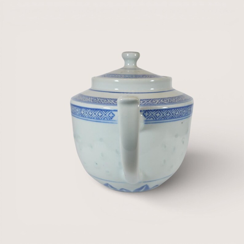 May include: A white porcelain teapot with a blue geometric pattern around the rim and on the lid. The teapot has a curved handle and a small knob on the lid. The design is a classic style, suitable for serving tea.