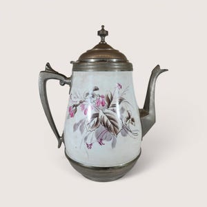 May include: Antique white and silver teapot with a floral design. The teapot features a silver handle, spout, and lid. The body of the teapot is white with a painted design of pink and brown flowers and leaves.