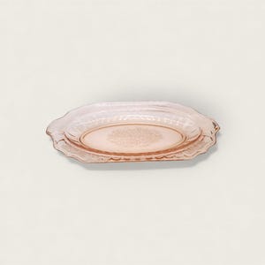 May include: A light pink, oval-shaped glass serving dish. The dish has a scalloped edge and a floral pattern in the center. The glass is translucent, and the dish appears to be vintage.