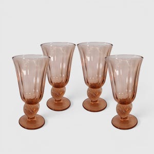 May include: A set of four matching pale pink glass goblets. Each goblet features a tall, fluted bowl with vertical ridges and a distinct twisted, spiral-patterned stem that connects to a smooth, circular base. The glass is translucent and uniform.