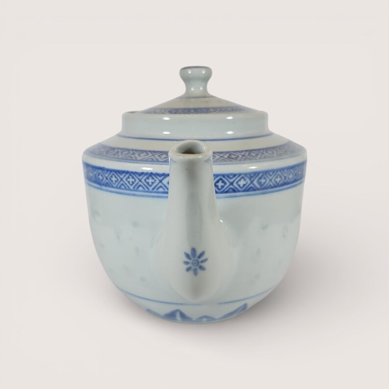 May include: A white porcelain teapot with a lid, featuring blue floral and geometric patterns. The spout has a small blue flower design. The teapot is a traditional shape, suitable for serving tea.