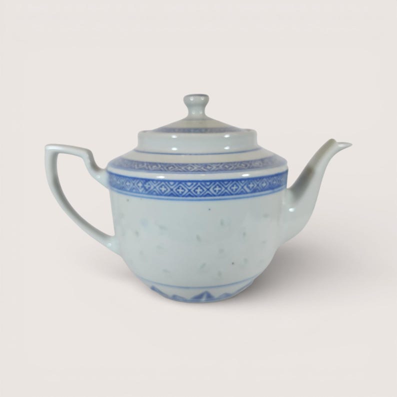 May include: White porcelain teapot with blue geometric patterns around the rim and lid. The teapot has a curved spout and handle, and a small knob on the lid. The body of the teapot has small, evenly spaced holes.