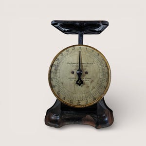 May include: An antique black Columbia Family Scale with a circular dial and a black pointer. The dial displays numbers from 0 to 23 pounds, with the text "24 POUND BY OZS" and "LANDERS, FRARY & CLARK, NEW BRITAIN, U.S.A."