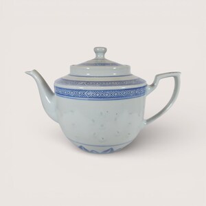May include: A white porcelain teapot with a lid, spout, and handle. The teapot features a blue geometric pattern around the body and lid. The teapot is a classic design, suitable for serving tea.