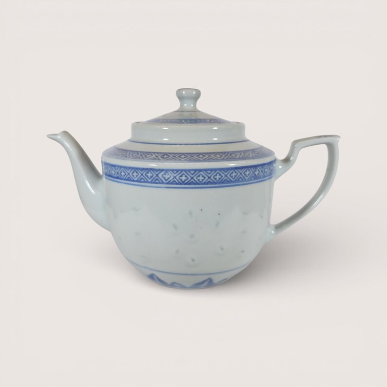 May include: A white porcelain teapot with a lid, spout, and handle. The teapot features a blue geometric pattern around the body and lid. The teapot is a classic design, suitable for serving tea.