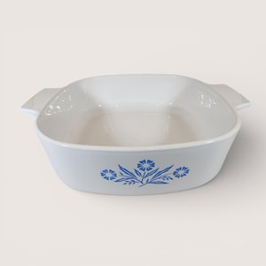 May include: A white and blue ceramic baking dish with a floral design. The dish has a square shape with rounded corners and two handles. The blue floral pattern is located on the front of the dish.