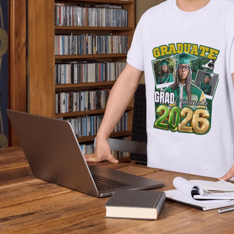 May include: White t-shirt with a graduation design. The shirt features the word "GRADUATE" in green and gold, along with the name "Amanda" and the year "2026". The design includes photos of a person in a graduation cap and gown.
