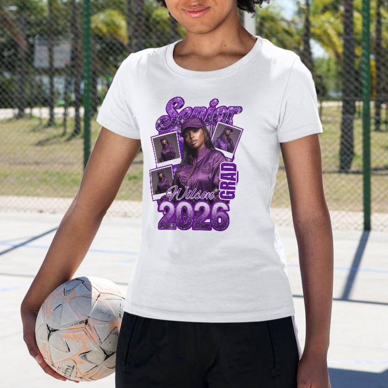May include: White t-shirt with a purple graphic design. The design includes the words "Senior Grad 2026" and a photo of a person in a purple outfit. The shirt is short-sleeved.
