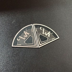 Könnte beinhalten: Zwei schwarze Halbkreis-Embleme aus Metall mit geometrischem Design und dem Wort "Club" in weiß.