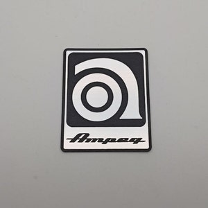 Op de afbeelding: Een zwart-witte logo sticker met een gestileerde "A" en het woord "Ampeg" in witte letters.