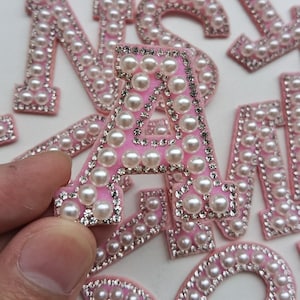 May include: Pink felt letter A with white pearl and rhinestone embellishments.