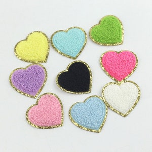 May include: Nine heart-shaped fabric patches with gold trim. The patches are in various colours, including pink, blue, yellow, green, white, and black.