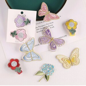 May include: Assortment of colorful embroidered iron-on patches featuring butterflies and flowers. The patches are perfect for adding a touch of whimsy to clothing, bags, or other accessories.