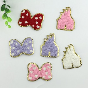 Puede incluir: Seis parches para planchar, tres son parches en forma de castillo de color rosa, morado y blanco con ribete de purpurina dorada, y tres son parches en forma de lazo de color rojo, morado y rosa con lunares blancos y ribete de purpurina dorada.