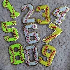 Peut inclure: Neuf chiffres en feutre de style baseball, chacun avec des coutures rouges, en jaune, blanc et vert néon. Les chiffres sont 1, 2, 3, 4, 5, 6, 7, 8 et 9.