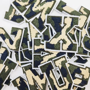 May include: A pile of felt letter patches in a camouflage pattern. The letters are in a variety of sizes and are all in uppercase. The patches are perfect for adding a touch of personality to clothing, bags, or other accessories.