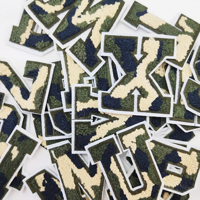 May include: A pile of felt letter patches in a camouflage pattern. The letters are in a variety of sizes and are all in uppercase. The patches are perfect for adding a touch of personality to clothing, bags, or other accessories.