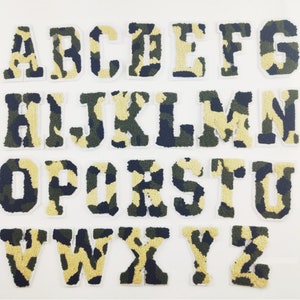 May include: A set of 26 iron-on patches featuring the alphabet in a camouflage pattern. The letters are white with a green, brown, and black camouflage design.