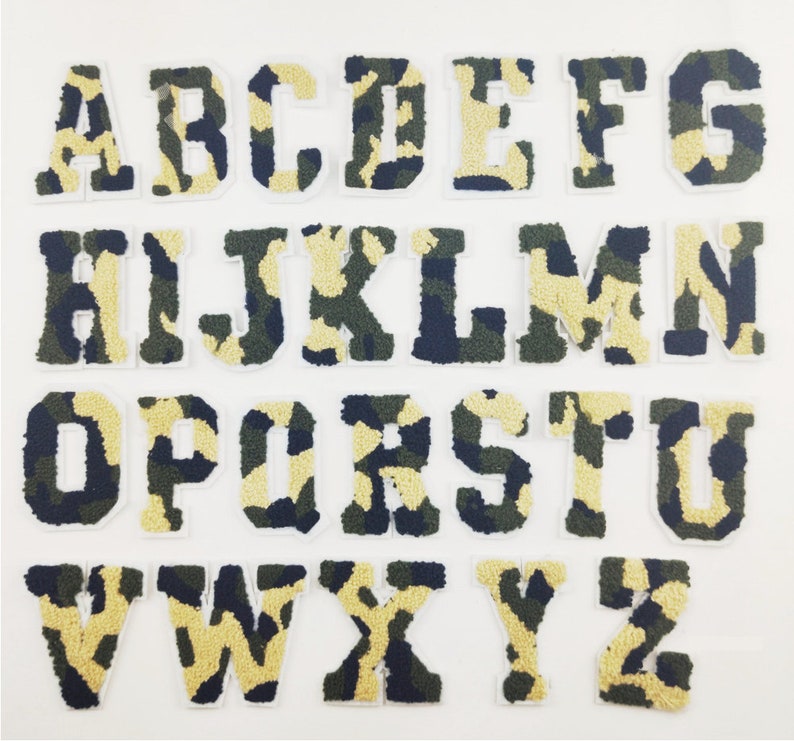 May include: A set of 26 iron-on patches featuring the alphabet in a camouflage pattern. The letters are white with a green, brown, and black camouflage design.