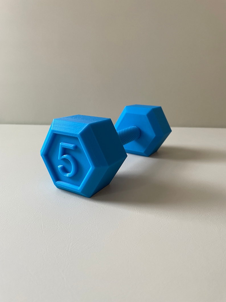 May include: A blue plastic dumbbell with a hexagonal shape and the number "5" printed on one side.