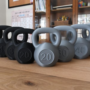 May include: A set of nine kettlebells, five gray and four black, arranged in a row on a wooden surface. The kettlebells are numbered 20, 30, 40, 50, and 60 pounds.